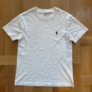 Vit t-shirt från Polo Ralph Lauren - Klassisk vit t-shirt från Polo Ralph Lauren med broderad marinblå logga på bröstet. T-shirten har rund hals, korta ärmar och är tillverkad i mjuk bomull. Perfekt basic-plagg med stilren design och skön passform. Är i storlek 140 barn men funkar som vanlig och skön t-shirt för XXS-XS-S!! Pris går alltid att diskuteras vid snabb affär!! Fler frågor går det bara att DM’a💕💕
