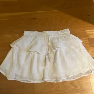 Vit volangkjol med knytband - Superfin vit kortkjol med volang och knytband med tofsar i midjan. Kjolen har en luftig känsla och resår i midjan för extra komfort. Perfekt för varma dagar och ger en fräsch och somrig vibe. Knappt använd, hör av dig vid frågor, lägg prisförslag 💕