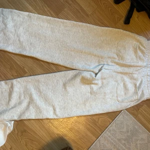 Ljusgrå mjukisbyxor från 157, stl S - Superbekväma ljusgrå mjukisbyxor från 157 med bred resår och snörning i midjan. Byxorna har raka ben, två stora fickor framtill och är gjorda i mjuk bomullsmix. Perfekta för chill eller träning.