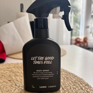 LUSH Let The Good Times Roll Body Spray - En svart sprayflaska med 200 ml body spray från LUSH, Let The Good Times Roll. Doften beskrivs som en explosion av smörig popcorn och karamell, perfekt för dig som gillar söta och unika dofter. Flaskan har en modern design med vit text och praktiskt spraymunstycke. Använd minst 5 gånger