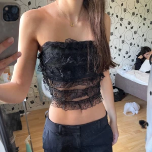 Svart bandeau tubtopp i spets - Säljer en svart bandeau tubtopp med flera lager volangig spets och mesh partier. Toppen är croppad och axelbandslös, perfekt för utgång eller fest. 