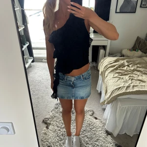Svart oneshoulder topp från Zara - Supersnygg svart oneshoulder topp från Zara med volangdetaljer och lätt rynkad struktur. Toppen är croppad och har en unik asymmetrisk design som verkligen sticker ut. Perfekt för dig som vill ha något trendigt och annorlunda i garderoben.