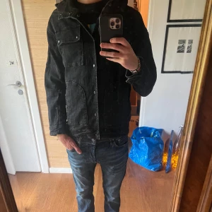 Svart jeansjacka med huva - Säljer en riktigt fet svart jeansjacka med huva och tryckknappar framtill. Jackan har stora fickor på sidorna och en bröstficka med lock. Snygg och enkel design som passar till det mesta. Jackan är inprincip nyskick. Passar medium/small