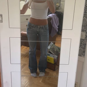 Blå bootcut jeans från Sweet S - Snygga blå bootcut jeans från Sweet S med låg midja och slitna detaljer. Jeansen har unika bakfickor med lock och rosa broderingar. Jeansen är köpte second hand så vet inte märket💕 Innerbenslängden: 84cm, midjemått: 37cm