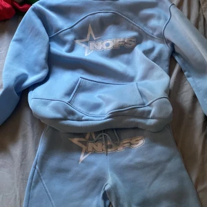 Ljusblå mjukisbyxor från NOFS - Säljer ett par ljusblå mjukisbyxor från NOFS med vit logga och stjärndetalj framtill. Byxorna har snörning i midjan och är gjorda i mjukt material som passar perfekt för chill dagar. Matchar med hoodie för en komplett look.