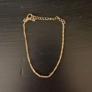 Tunt guldarmband med kedja - Säljer ett stilrent och tunt armband i guldton med tvinnad kedja och justerbar längd. Perfekt för dig som gillar minimalistiska smycken och vill ha något diskret men ändå snyggt på handleden. Mycket bra skick