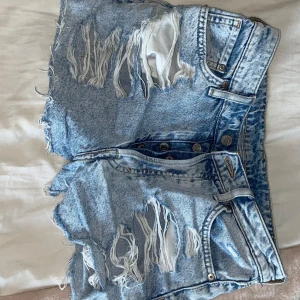 Vintage högmidjade jeansshorts - Snygga vintage-inspirerade jeansshorts i ljusblå denim med hög midja. Shortsen har slitna detaljer och fransiga kanter. 
