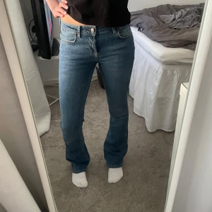 Low Waits jeans - Säljer ett par klassiska blå jeans med bootcut-snitt och låg midja. Jeansen har fem fickor, dragkedja och knapp framtill. De är i ett mjukt denimtyg som sitter snyggt över höfterna och har en lätt utsvängd passform nertill.