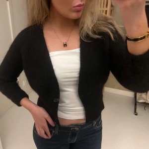 Svart stickad kofta med knappar - Säljer en svart, croppad stickad kofta med två knappar framtill. Koftan har lång ärm och en enkel, klassisk design som är lätt att matcha. Perfekt för lager-på-lager och funkar året runt❤️