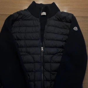 Moncler cardigan (svart) - Svart Moncler tricot cardigan i fint skick. Perfekt till hösten som kommer eller nu på sommarkvällar. Säljer pga att den blivit för liten. Jackan är i M och sitter bra på en person mellan 180-165 cm. Hör gärna av er om ni har några funderingar! 😁🧥