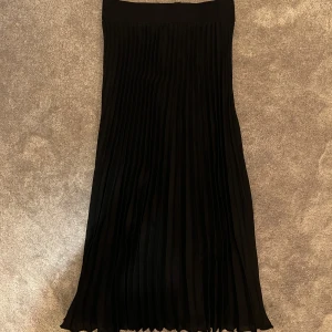 Svart plisserad långkjol - Snygg svart långkjol med plisserade veck och bred midja. Kjolen har ett stilrent och klassiskt uttryck som passar perfekt till sneakers eller boots. Enkel att matcha med både stickade tröjor och crop tops.