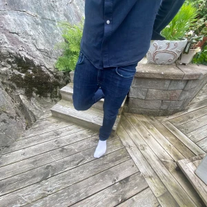 Nudie slim jeans herr - Säljer ett par mörkblå nudie slim jeans med klassisk femficksdesign och snygga sömmar. Jeansen har en smal passform och är tillverkade i stretchigt denim för extra komfort. Perfekta för dig som gillar en tajt look och vill ha ett par stilrena jeans i garderoben. Det finns en liten defekt under gylfen men syss lät ihop.