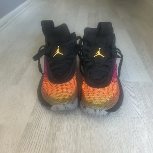 Nike Jordan sneakers i svart och färgskiftning - Snygga Nike Jordan sneakers med svart ovandel och färgskiftande mesh i orange, rött och lila. Skorna har gula detaljer och logga, samt mönstrad sula med bra grepp. Perfekta för dig som vill sticka ut med coola färger och sportig vibe.