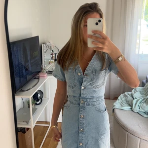 Ljusblå jeansklänning med knappar - Säljer en ljusblå jeansklänning med kort ärm och knappar hela vägen framtill. Klänningen har två bröstfickor och två bakfickor, markerad midja och en snygg v-ringning. Perfekt för dig som gillar en avslappnad men trendig look.