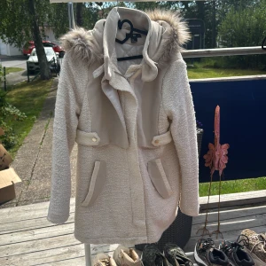 Beige teddyjacka med fuskpäls H&M - Supermysig beige teddyjacka från H&M med huva och fuskpälsdetalj. Jackan har långa ärmar, knappar och dragkedja framtill samt praktiska fickor med snygga detaljer. Perfekt för kyliga dagar när du vill vara både varm och stylish.