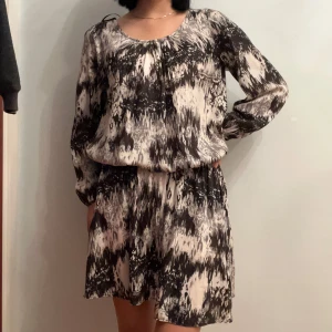 Mönstrad kortklänning från Gina Tricot - Supersnygg kortklänning från Gina Tricot med abstrakt svart och beige mönster. Klänningen har långärmade ärmar, rund halsringning och ett avslappnat fall. Perfekt för dig som gillar unika prints och en skön, luftig känsla. Den sitter åt vid midjan så du kan anpassa hur kort/lång den ska vara!✨ sparsamt använd, finns en extra knapp som följer