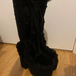 Demonia Camel 311 - Unika svarta boots från märket demonia (camel 311) med hög platå och chunky klack. Skorna är täckta av mjuk päls och har snörning framtill samt dragkedja på sidan .Materialet är mockaliknande och pälsigt. Dom kom aldrig till användning så helt nytt skick
