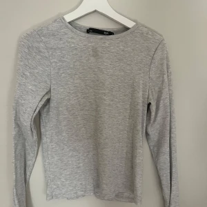 Ljusgrå långärmad tröja från 157 - En basic ljusgrå långärmad tröja från 157. Enkel och clean design med rund halsringning och mjukt material som känns skönt mot huden. Perfekt att styla med jeans eller under en jacka. Passar dig som gillar minimalistisk stil.
