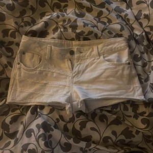 Vita lågmidjade shorts med spetsdetaljer - Snygga vita lågmidjade shorts från Gina Tricot i storlek 34. De har klassisk femficksdesign och coola spetsdetaljer framtill som ger en extra touch. Perfekta för varma dagar och riktigt fräsch look. Materialet är bomull med lite stretch för skön passform.