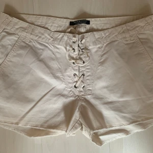 Vita shorts med snörning Maison Scotch - Snygga vita shorts från Maison Scotch med cool snörning framtill och råa kanter. Shortsen har fickor fram och bak, samt en liten metallblomma som detalj vid fickan. Säljer pga att de är för stora!