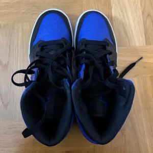 Nike Air Jordan 1 svart/blå sneakers - Säljer ett par snygga Nike Air Jordan 1 sneakers i svart och blått skinn med klassisk vit sula. Skorna har svarta snören, hög modell och Air Jordan-loggan på sidan. Använda endast 1 gång och i ett perfekt skick, därav priset