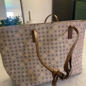 Beige shoppingväska By Malene Birger - Stor shoppingväska från By Malene Birger i beige och grått med klassiskt rutigt mönster. Väskan har bruna handtag i skinn och en innerficka med dragkedja. Perfekt för dig som vill ha plats för allt och gillar stilren design. Handtagen är slitna men funkar nog att limma till lite