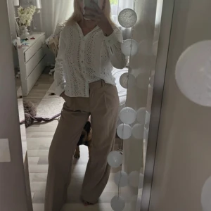 Beiga vida kostymbyxor - Snygga beiga kostymbyxor med hög midja och vida ben. Byxorna har klassisk look med pressveck och sidfickor. Perfekta att styla med en skjorta eller crop top för en clean vibe.