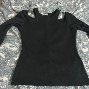 Svart långärmad topp med cut-outs - Svart långärmad topp från Zara med trendiga cut-outs vid axlarna och smala band som detalj. Tight passform och rund halsringning. Passar även en XS