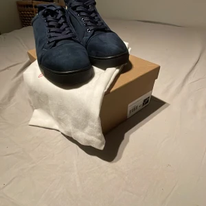 Mörkblå sneakers från Christian Louboutin - Snygga mörkblå sneakers från Christian Louboutin i mocka med ton-i-ton broderad logga på hälen. Skorna har rund tå, blåa snören och svart platt sula. Insidan är i ljust skinn och de kommer med originalkartong, dustbag och äkthetsbevis.