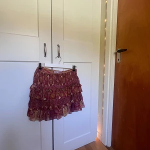Kjol från Zara - Supersöt kort kjol från Zara med volanger och bohemiskt mönster i vinrött, gult och rosa. Endast använt fåtal gånger, storleken är M men den passar mig som vanligtvis har XS🧡