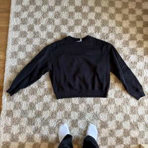 Svart croppad sweatshirt från Weekday, S - En svart sweatshirt från Weekday i storlek S. Tröjan har en klassisk rund halsringning, ribbade muddar och en något boxig passform. Obs. Den är croppad så alltså kortare i längden.