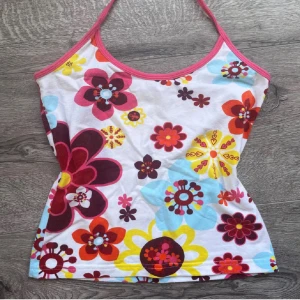 Färgglad blommig linnetopp - Superfin linnetopp med stora blommor i rött, gult, blått och orange på vit botten. Smala axelband och rosa kant runt halsen ger en söt och somrig känsla. Perfekt för dig som gillar färg och retrovibbar!