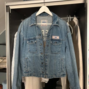 Jeansjacka från Superdry med brodyr - Snygg blå jeansjacka från Superdry med broderad text i vitt och guld på ryggen. Storlek M men passar även de som har storlek S💙🩵