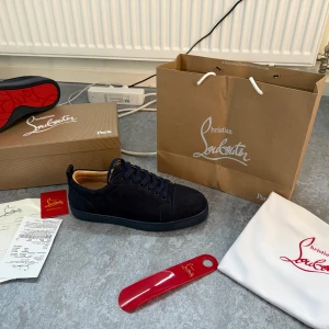 Mörkblå sneakers från Christian Louboutin - Snygga mörkblå sneakers från Christian Louboutin i mocka med klassisk röd sula och broderad logga på hälen. Skorna har rund tå, platt sula och matchande mörkblå snörning. Perfekta för dig som vill ha en lyxig och stilren look.
