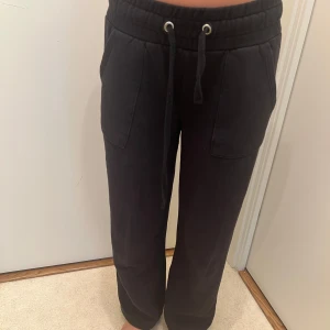 Svarta mjukisbyxor med snörning - Svarta mjukisbyxor med bred resår i midjan och snörning framtill. Byxorna har två stora fickor fram och ett avslappnat, rakt snitt som ger en loose passform. Perfekta för chill dagar eller när du vill vara extra bekväm.