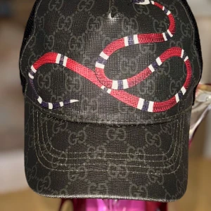 Gucci Original Keps – Kingsnake Design - Exklusiv och trendig Gucci-keps i svart med det ikoniska GG Supreme-mönstret och den välkända Kingsnake-ormen i rött, vitt och svart framtill med justerbar passform baktill för maximal komfort. Storlek M – Omkrets: 57 cm ✔ 100% original Gucci ✔ Ikonisk streetwear-look ✔ Perfekt för både vardag och statement-outfits  📦 Skickas snabbt och väl skyddad! 
