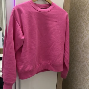 Rosa sweatshirt från NA-KD i bomull endast använd en gång  - Säljer en rosa sweatshirt från JXX i storlek XS. Tröjan har en klassisk rund hals, långa ärmar och är tillverkad i mjuk bomull. Perfekt för dig som gillar färgstarka och enkla plagg. Diskret logga på bröstet och ribbade muddar vid ärmslut och nederkant. Endast använd en gång