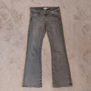 Grå bootcut jeans från Gina Tricot - Snygga grå jeans från Gina Tricot med bootcut och backfickor med knapp. Jeansen har låg midja och har "kontrastsömmar". Perfekta för dig som gillar en avslappnad och trendig stil.