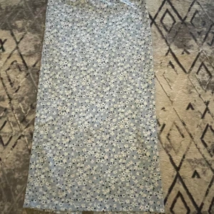 Blommig blå långkjol med slits - Säljer en blå långkjol med vitt blommigt mönster. Kjolen har en snygg slits bak på kjolen. Perfekt för dig som gillar mjuka material och somriga färger. 