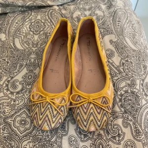 Gula flats/balerina skor - Gula flats/balerinaskor i ett fint mönster med en rosett från Tamaris. Aldrig använda och köpa för 50 kr