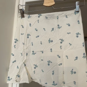Vit blommig kortkjol från ASOS DESIGN - Supersöt vit kortkjol från ASOS DESIGN med ljusblått blommigt mönster. Kjolen har en enkel och rak form, mjukt material. Oanvänd 