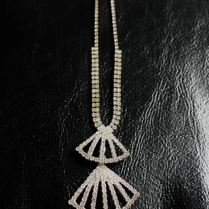 Glittrigt halsband med strass och geometrisk hänge - Supersnyggt halsband med dubbla rader av glittrande strass och ett unikt geometriskt hänge i solfjäderform. Perfekt för dig som vill sticka ut med extra bling! Kedjan är silverfärgad och hela smycket glittrar maxat i ljuset.