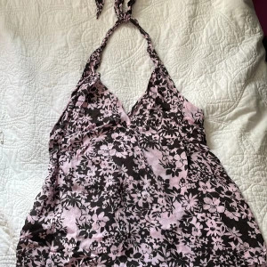 Blommig rosa linne kortklänning Benetton - Supersött linne från United Colors of Benetton med rosa och svarta blommor. Halterneck med knyt i nacken och v-ringad front. Lätt och luftig känsla, perfekt för varma dagar. Dragkedja i sidan för enkel påklädning. Passar dig som gillar romantisk och feminin stil.