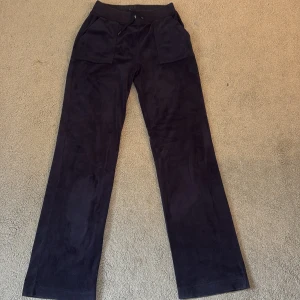 Svarta mjukisbyxor Juicy Couture XS - Svarta mjukisbyxor från Juicy Couture i storlek XS. Byxorna har raka ben, bred resår i midjan med snörning och stora fickor både fram och bak med knappdetaljer. Materialet är mjukt och har en lyxig känsla, perfekt för chill dagar.