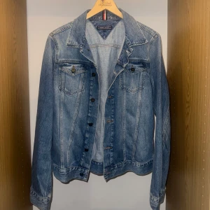 Blå jeansjacka Tommy Hilfiger - Snygg blå jeansjacka från Tommy Hilfiger med klassisk krage, bröstfickor med knappar och detaljerade sömmar. Jackan har en normal passform och är tillverkad i slitstarkt bomullsmaterial. Perfekt för dig som gillar en tidlös och cool streetstil.