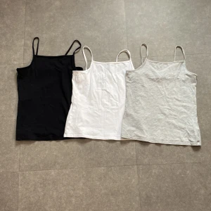 3-pack linnetoppar H&M svart, vit, grå - Tre stilrena linnetoppar från H&M i storlek 146/152. En svart, en vit och en ljusgrå, alla med smala axelband och rak passform. Perfekta att matcha med jeans eller shorts. Materialet är mjuk bomull. 💕