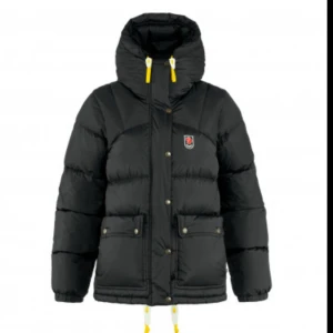 Svart dunjacka från Fjällräven - Säljer en svart dunjacka från Fjällräven med gul snörning i huvan och snygga detaljer. Jackan har två stora fickor framtill, tryckknappar och dragkedja. Perfekt för kalla dagar och har en cool, puffig look med Fjällräven-logga på bröstet. Köpt ett år sen ungefär men använd ca 10 gånger. Säljer pga för stor och kommer ej till användning, inte min smak i jackor. Storlek XXS men skulle passa allt från xxs/s 