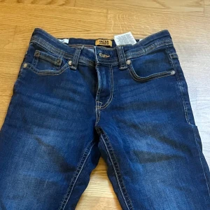Mörkblå jeans från Jack & Jones - Snygga mörkblå jeans från Jack & Jones med klassisk femficksdesign och kontrastsömmar. Modellen har normal passform och raka ben, tillverkade i mjukt jeansmaterial med lite stretch för extra komfort. Perfekt för dig som gillar stilrena och tidlösa jeans.