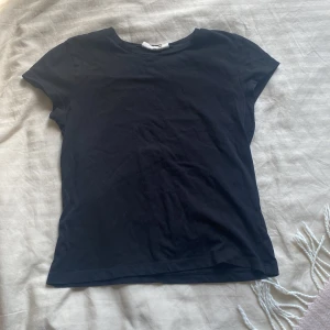 Svart enkel kortärmad topp - En stilren svart topp från kaphal med rund hals och korta ärmar. Modellen är klassisk och har en figurnära  passform som funkar till många olika looks. Materialet är mjuk bomull som känns skönt mot huden. Perfekt att matcha med jeans eller kjol för en clean vibe❣️