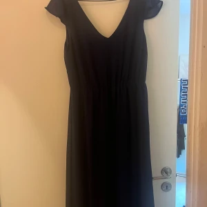 Marinblå balklänning - Snygg marinblå långklänning med djup v-ringning och korta ärmar. Klänningen har ett markerat midjeparti som ger en schysst siluett. Materialet känns lätt och flowy, perfekt för dig som gillar stilrena och enkla plagg med lite extra elegans. Helt oanvänd.